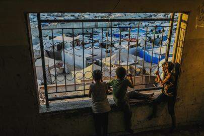 Ontheemde Palestijnse kinderen kijken vanuit een raamgat naar hun tentenkamp in Khan Younis.