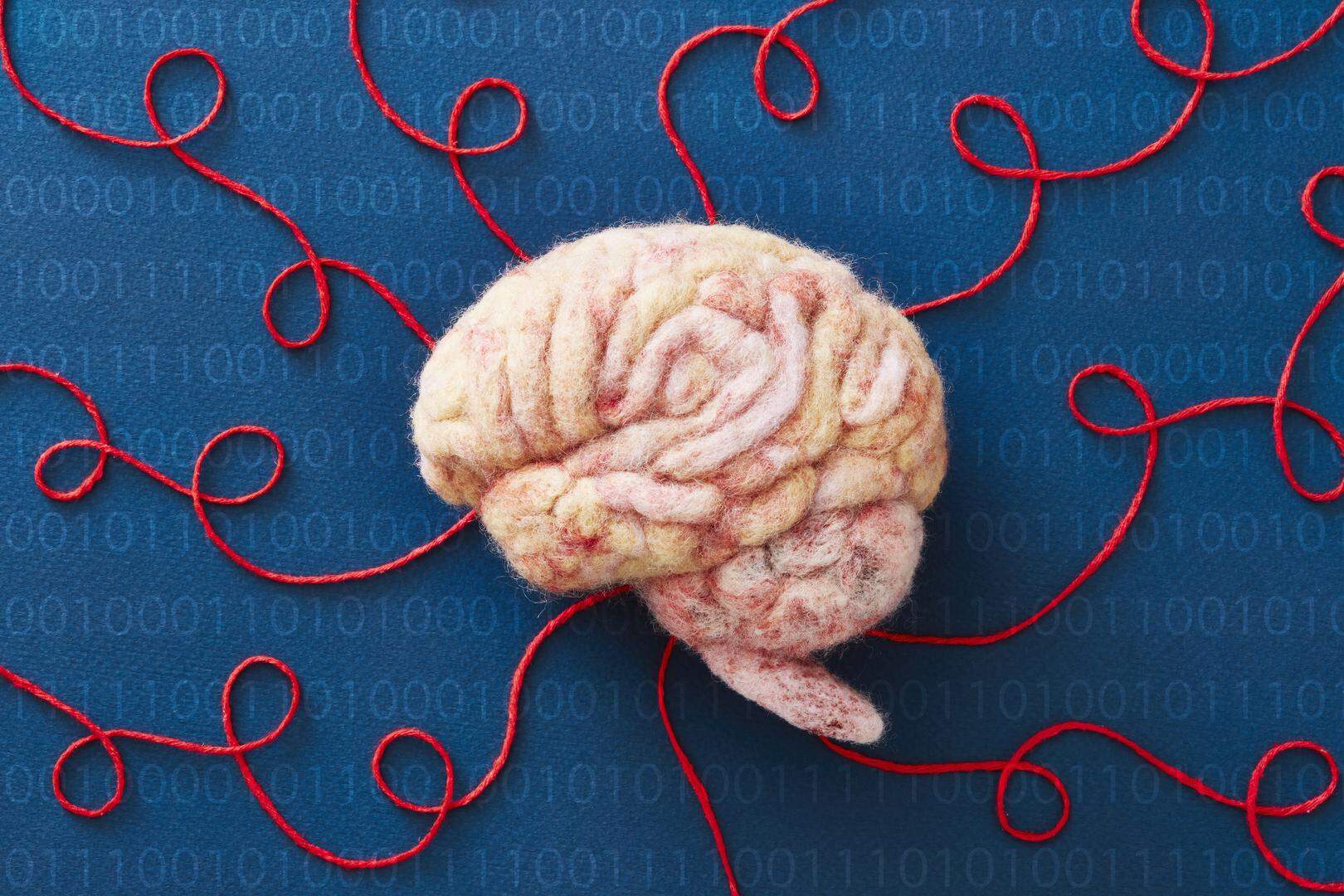 A human brain model made of wool with red string representing neural pathways