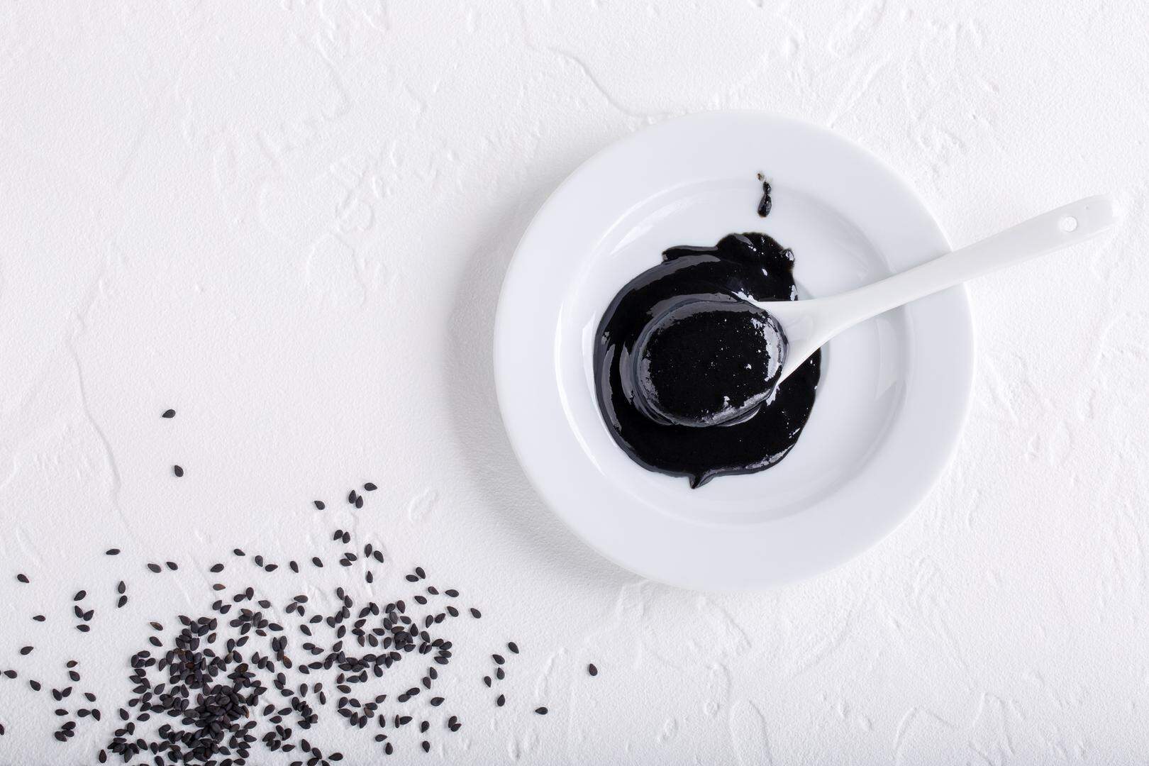 Black tahini sauce and black sesame seeds on white background. Natural paste made from sesame seeds. Copy space. Top view.