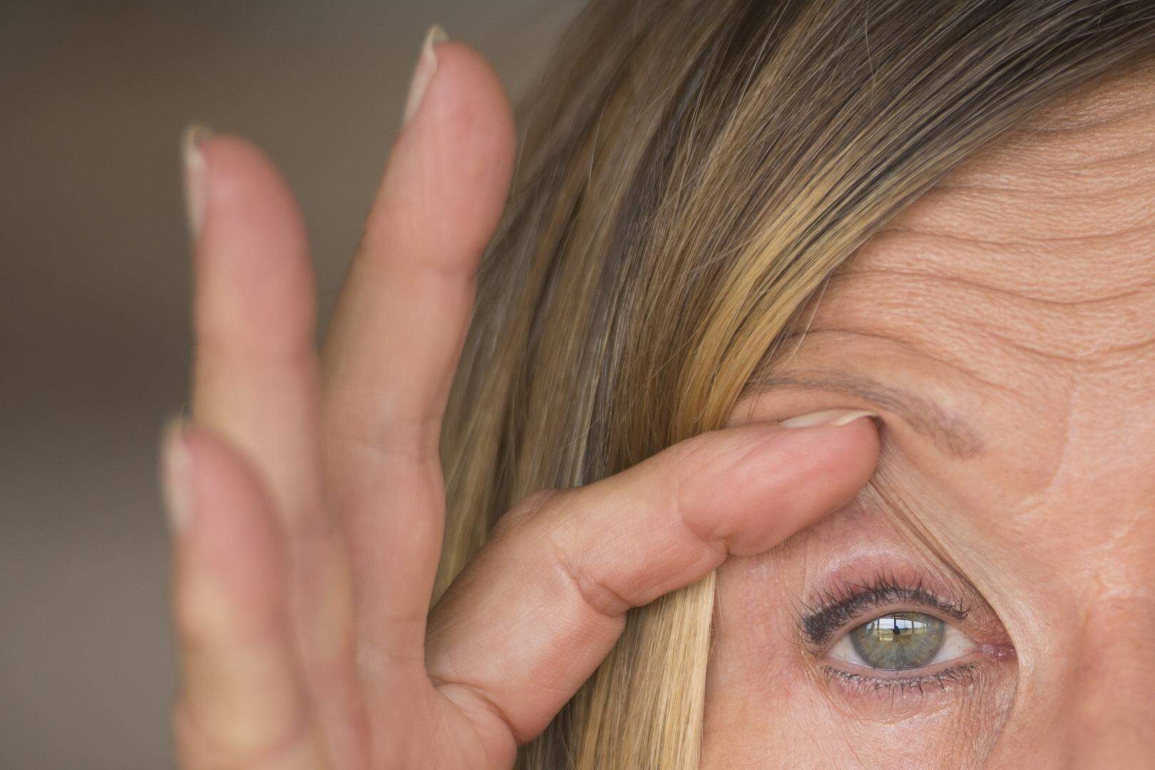 Portrait of attractive mature woman with tired and stressed facial expression, fingers keep eyes open, suffering migraine and headache, blurred background.