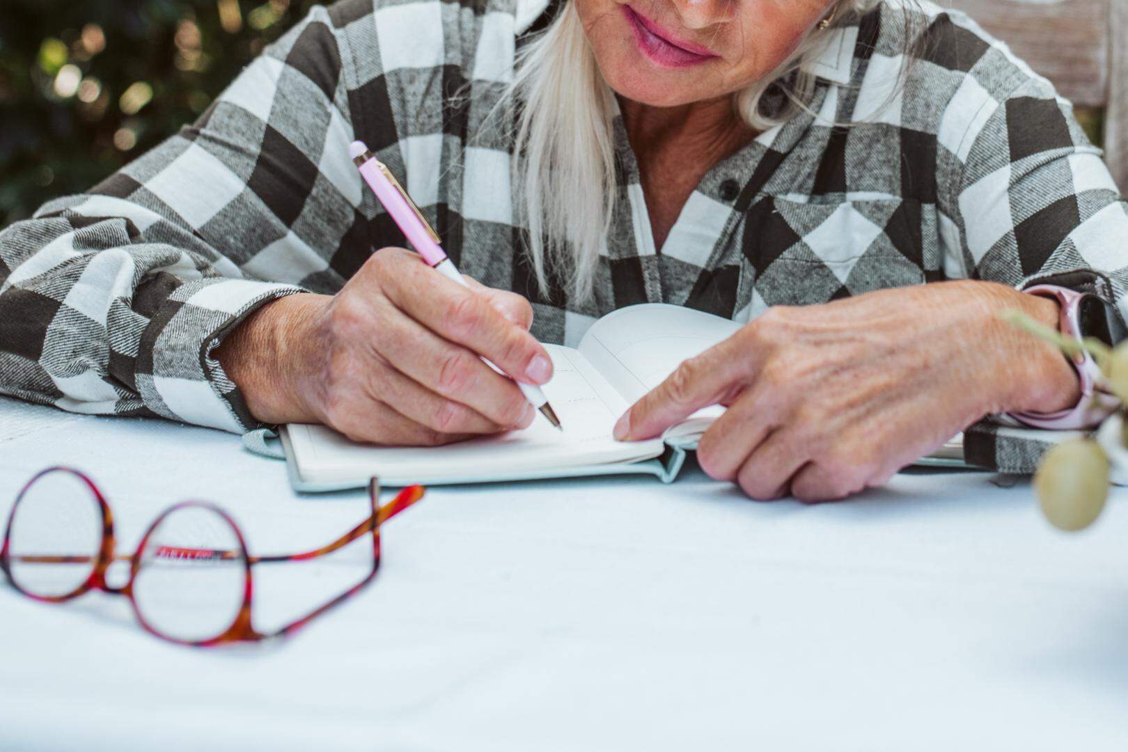 Beautiful older women is sitting in the garden and writing in her diary. Female senior is keeping daily journal, writing down thoughts and feelings