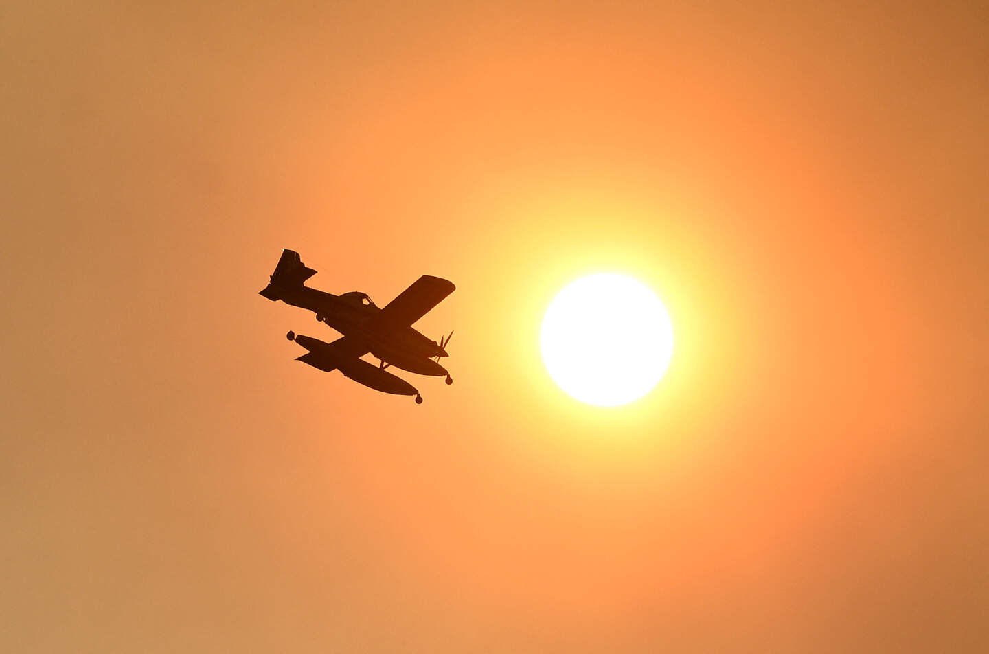 This picture taken on July 26, 2026 shows a firefighting aircraft with the sun in background during a wildfire near Vilavella, 50 kms north of Valencia. Spanish firefighters today battled a new front of fires near the coastal city of Valencia, where at least 15,000 people were evacuated. Spain has already evacuated tens of thousands of people from villages west of the capital Madrid where extremely dry conditions have been worsened by heatwaves and strong winds. In the Valencia region, on Spain's eastern coast, authorities said they were struggling to contain fires. (Photo by Jose JORDAN / AFP)