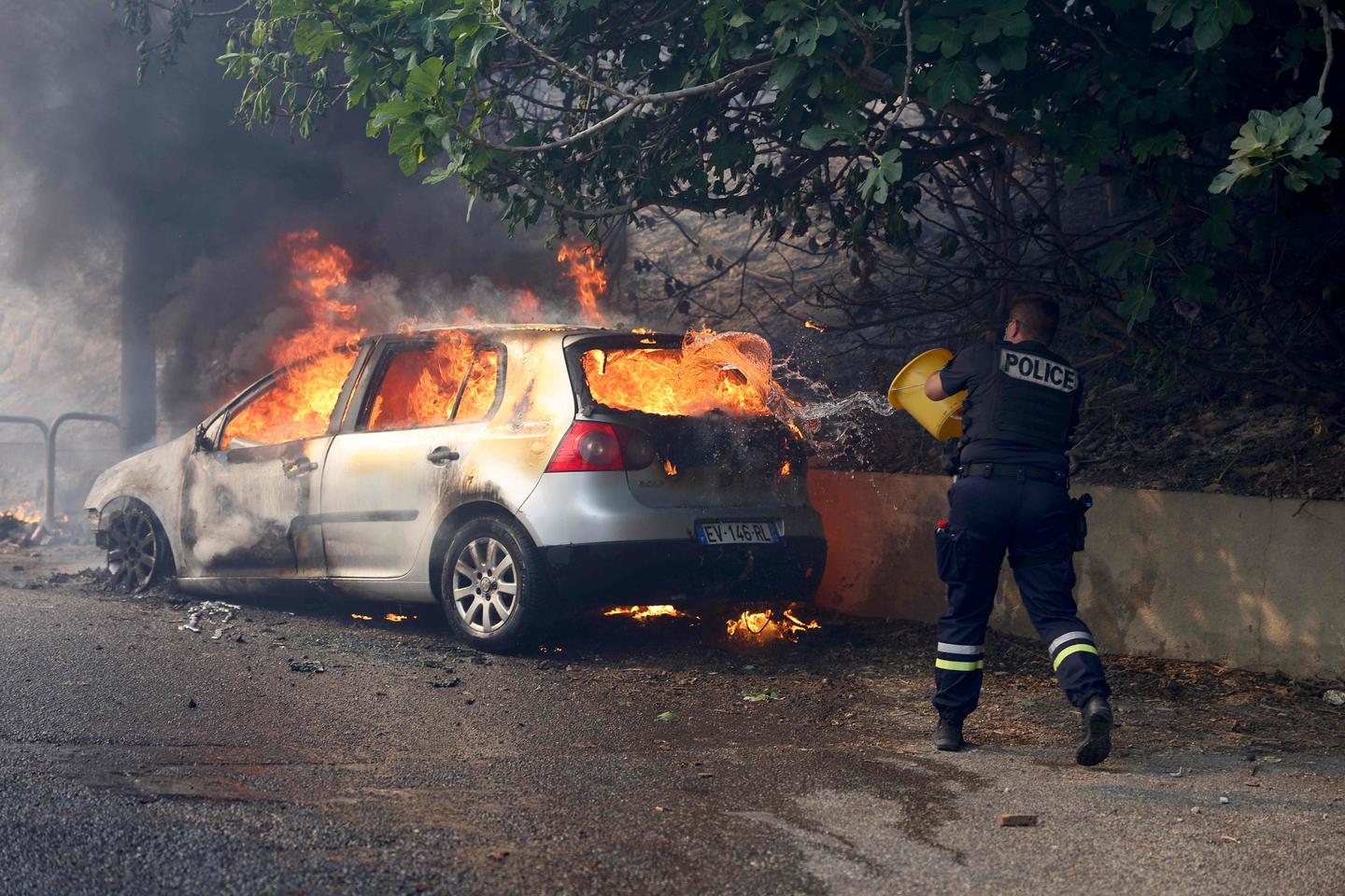 Een politieagent probeert een brand te blussen in een auto in de wijk L’Estaque in Marseille.