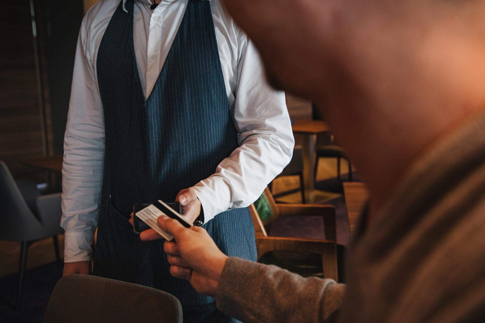Unrecognizable man using a credit card contactless method to pay a bill at a restaurant.